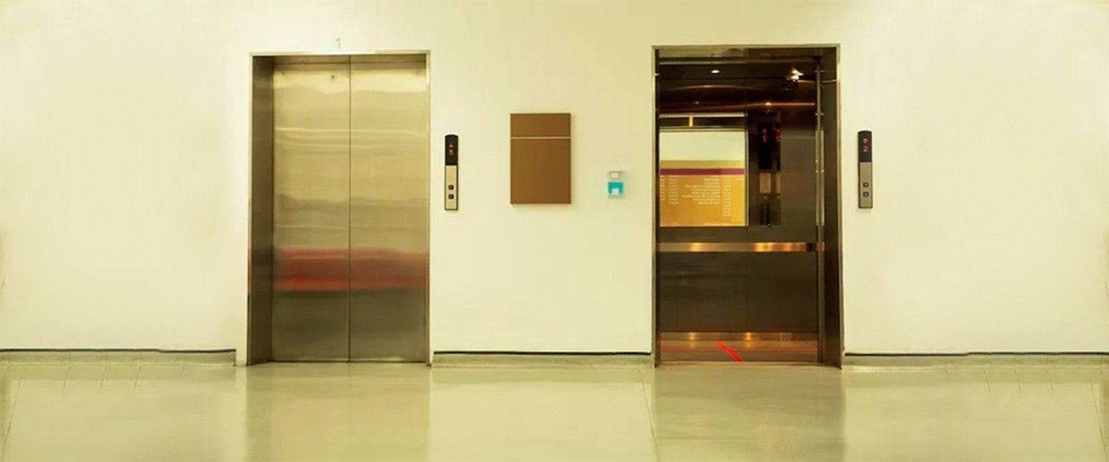 Two passenger elevators in a bright, modern building lobby, showing one closed lift and one open lift with control panels, highlighting Morden elevators in Hyderabad for modern properties.